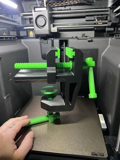 Peça verde e preta em produção na mesa de uma impressora 3D