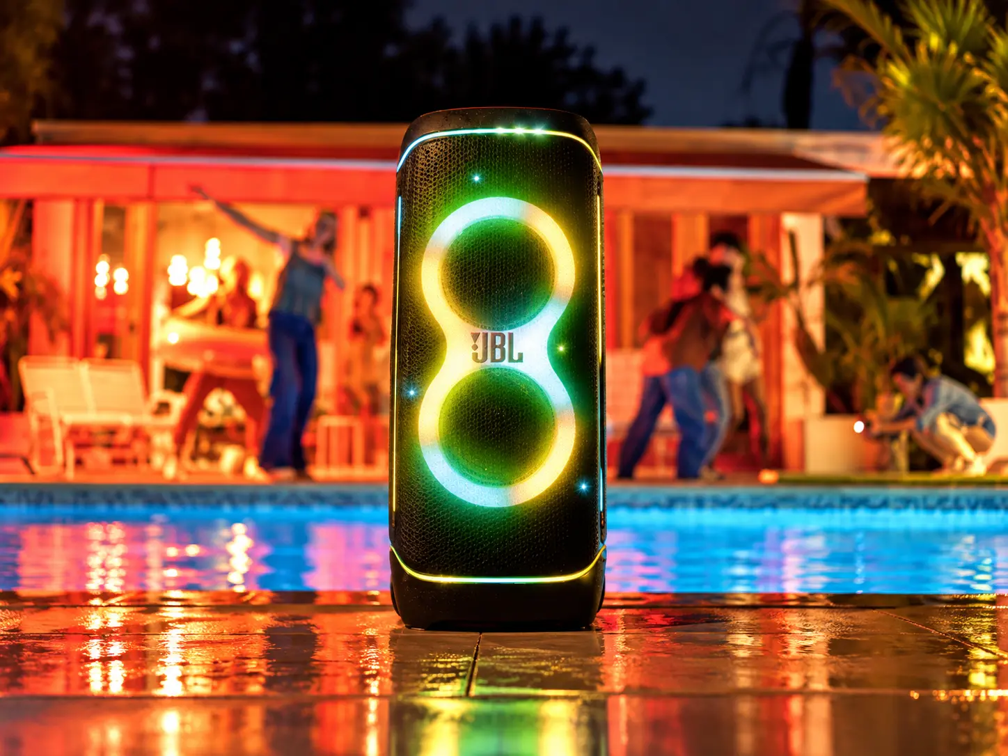 Caixa de som JBL com iluminação, em uma ambientação de festa à beira da piscina